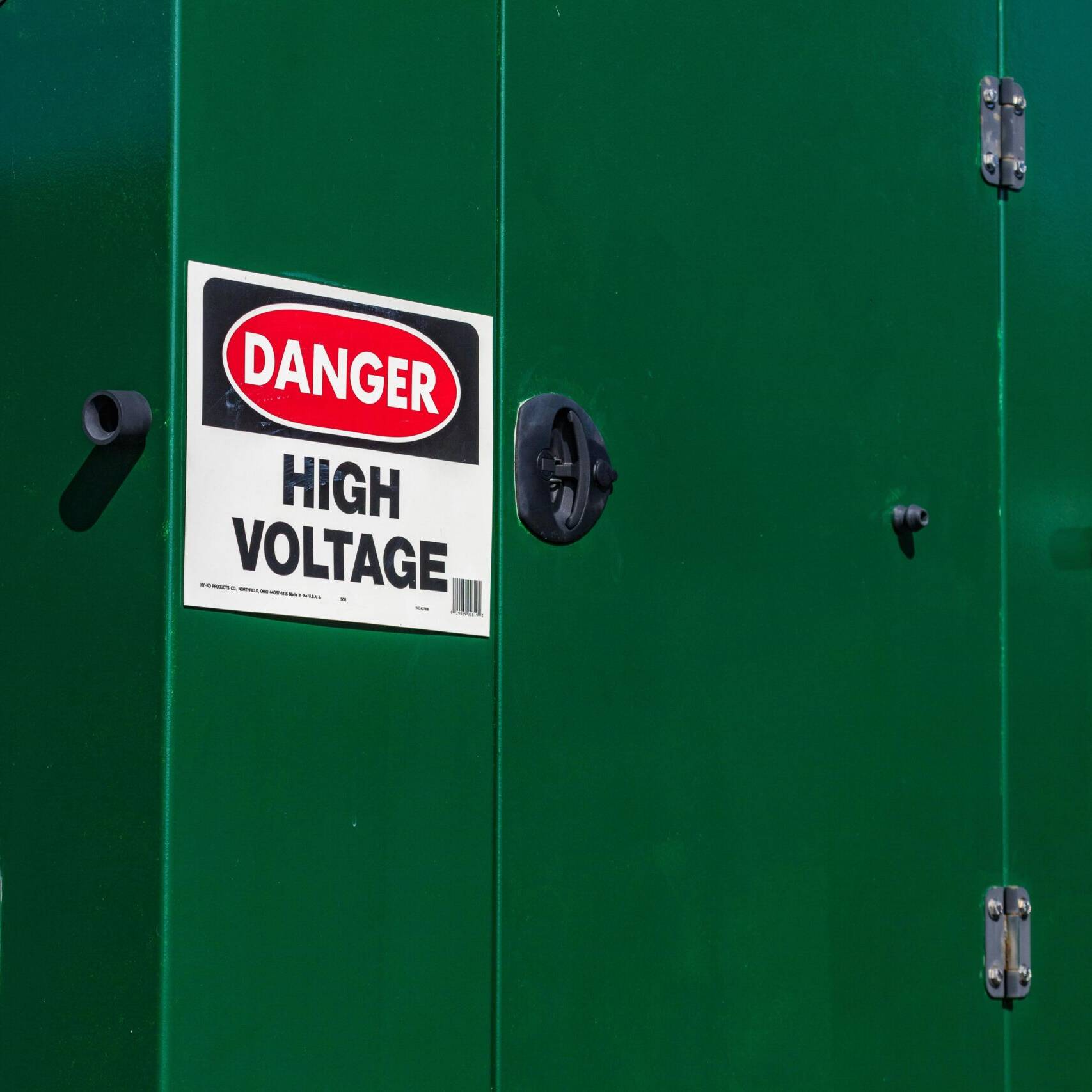 A sign on a green steel wall warning people of high voltage