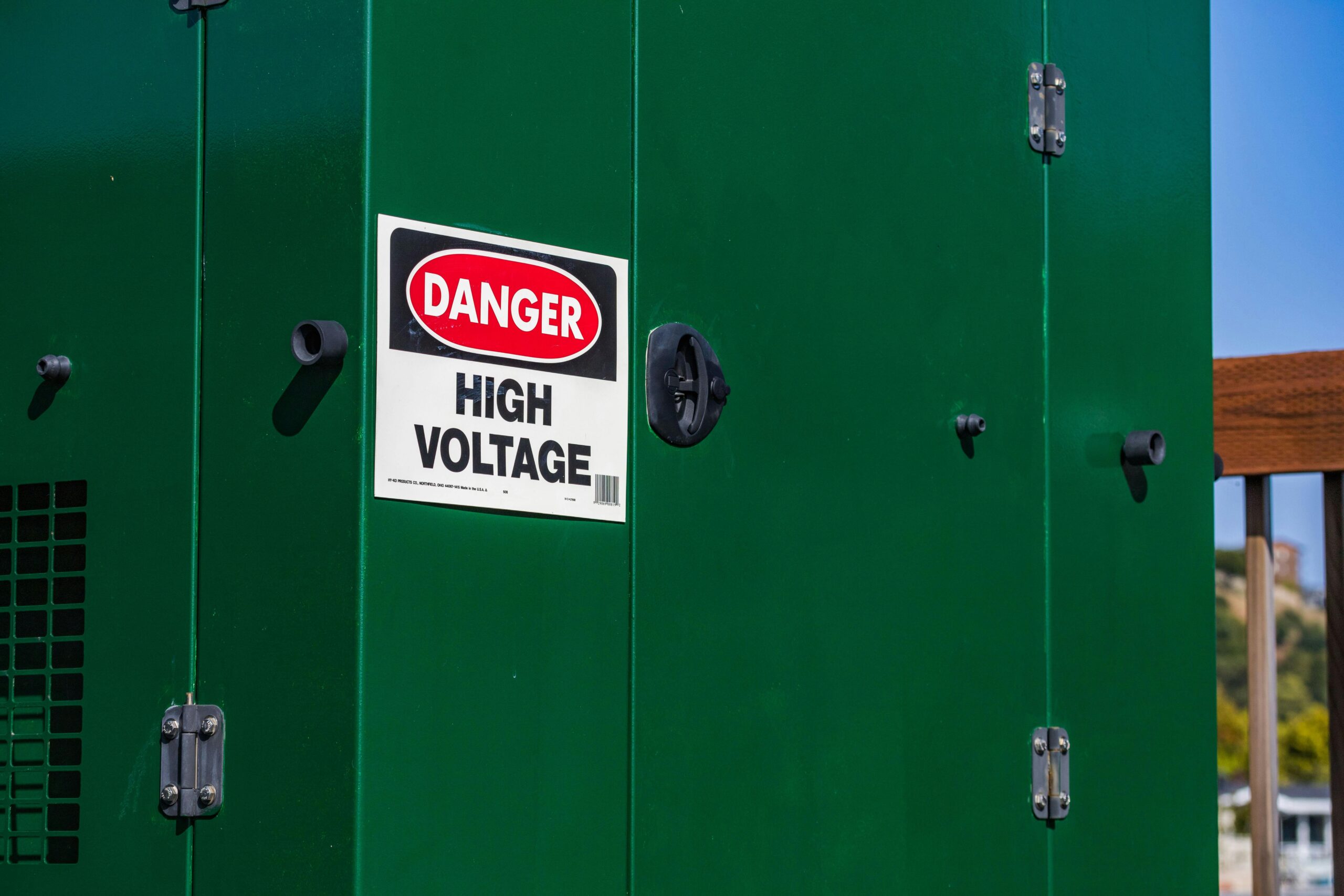 A sign on a green steel wall warning people of high voltage