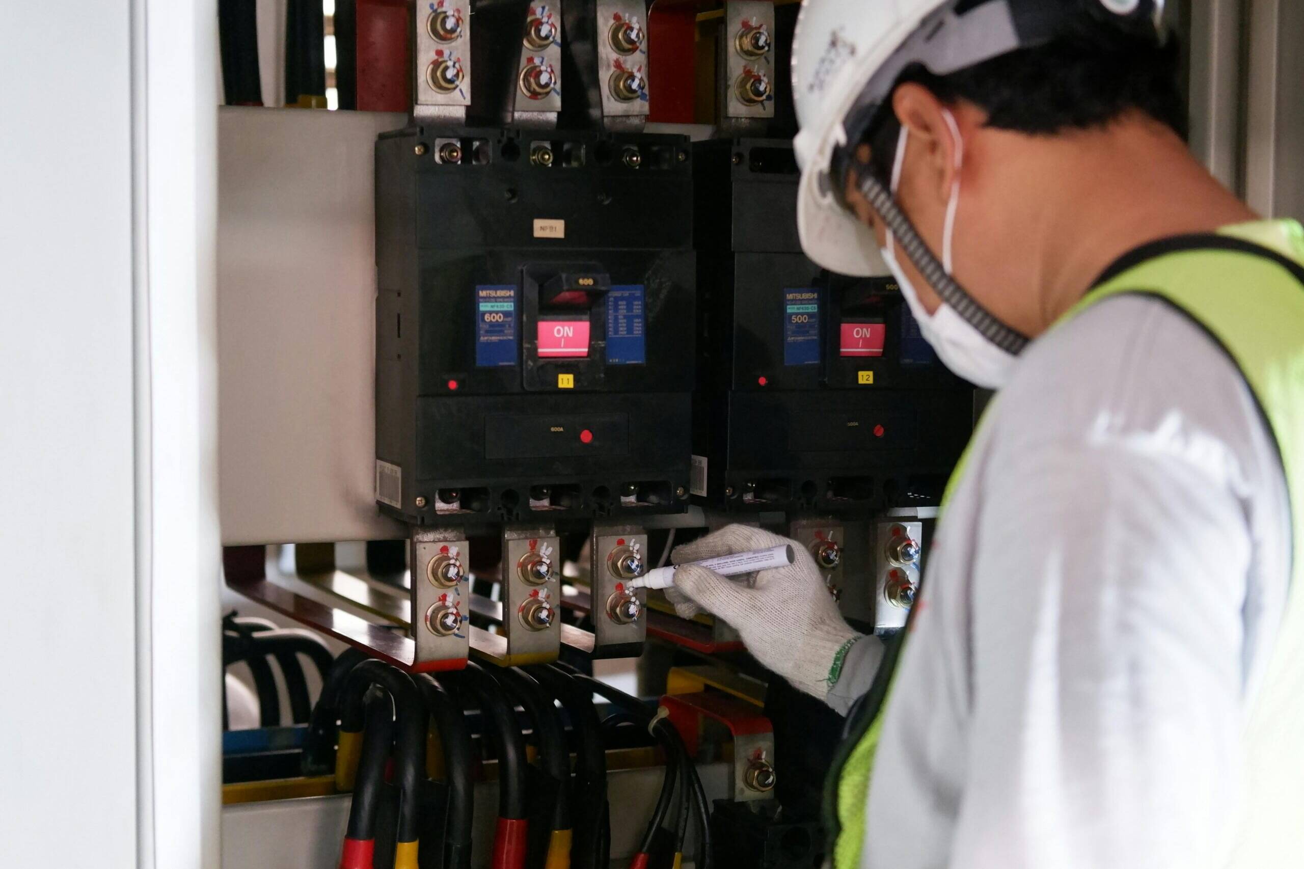 A man working in an electrical box with a hard hat and mask on.