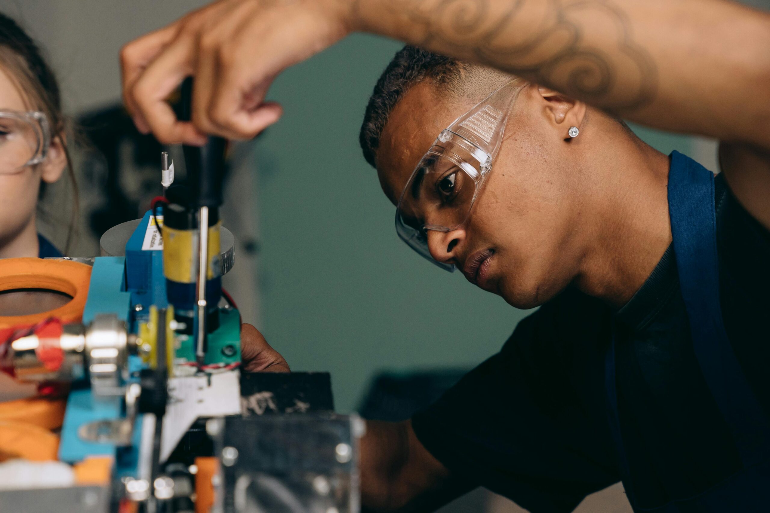 Engineer wearing safety goggles carefully assembling or adjusting a piece of industrial equipment in a workshop or lab environment.